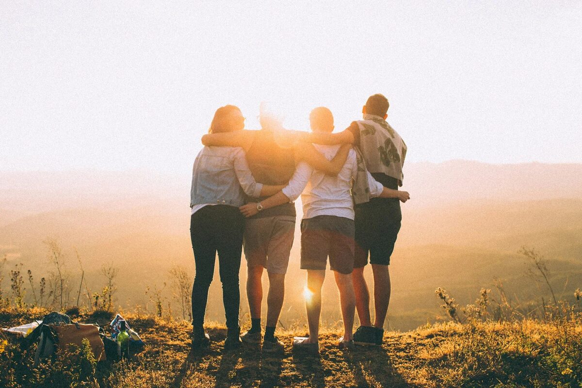 Five friends with arms around each other watching the sunset